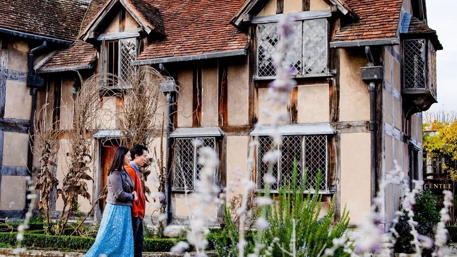 Woman in blue dress standing before Tudor-style timber-framed cottage with white panels