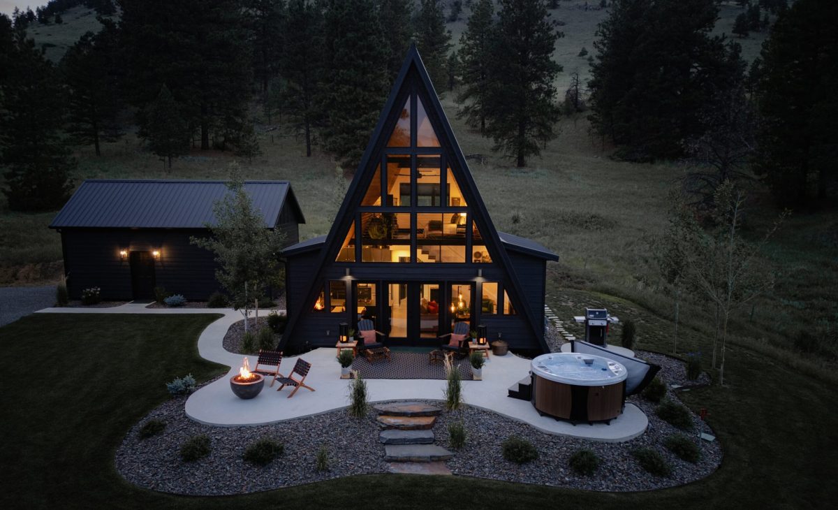 A-frame cabin with warm glowing windows nestled in a forested mountain setting at dusk