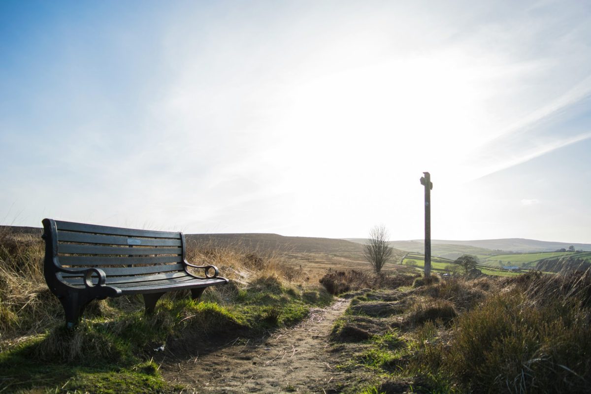 Wooden bench on a moorland path with rolling hills and a stone marker in Yorkshire