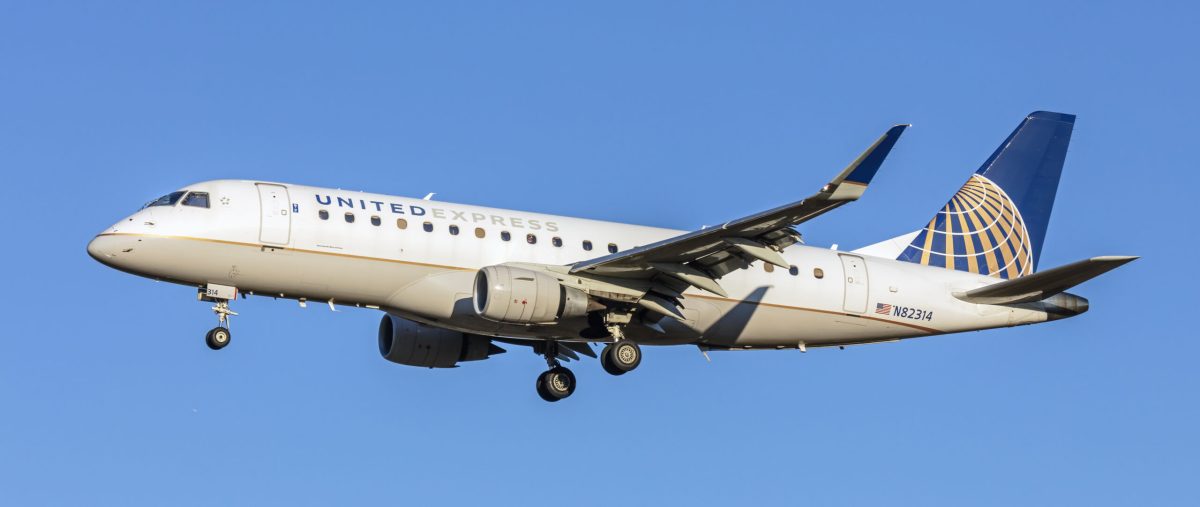 United Express regional jet in flight against a clear blue sky.