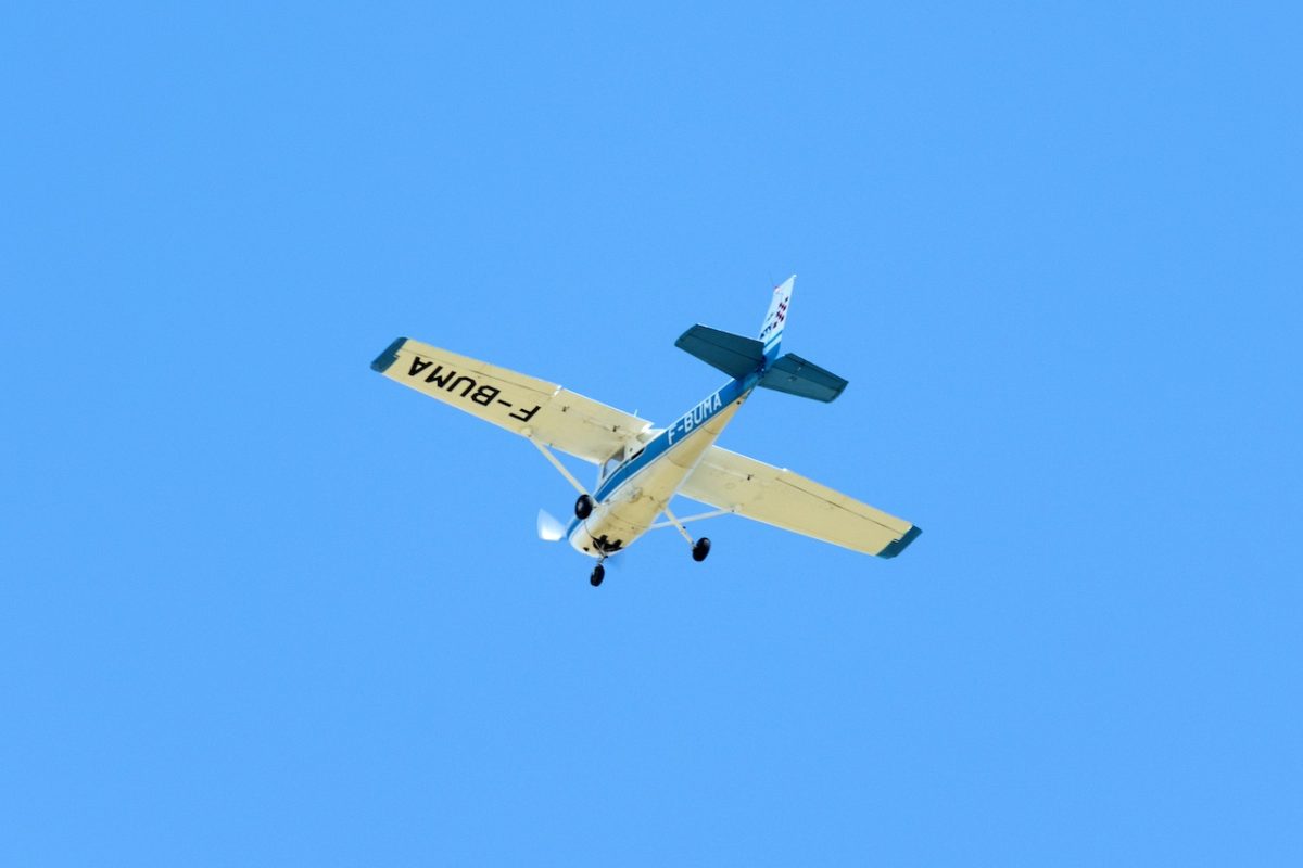 Small yellow and blue aircraft in flight against clear blue sky