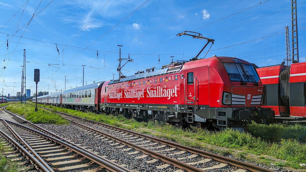 Red Scandinavian railway train on tracks with overhead electrical lines under blue sky
