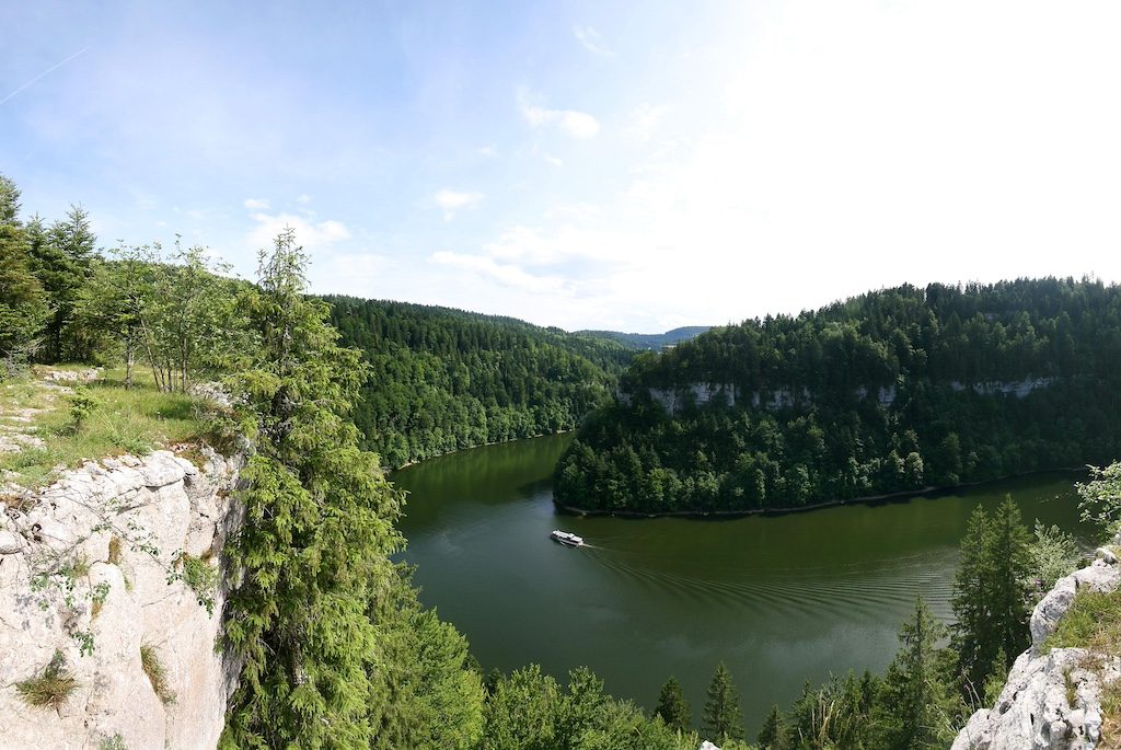 Alpine lake surrounded by forested mountains and rocky cliffs under blue sky