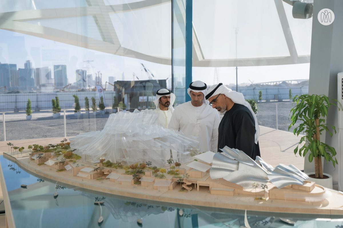 Three men examine architectural model of Dar al-Funoon with Abu Dhabi skyline visible through windows