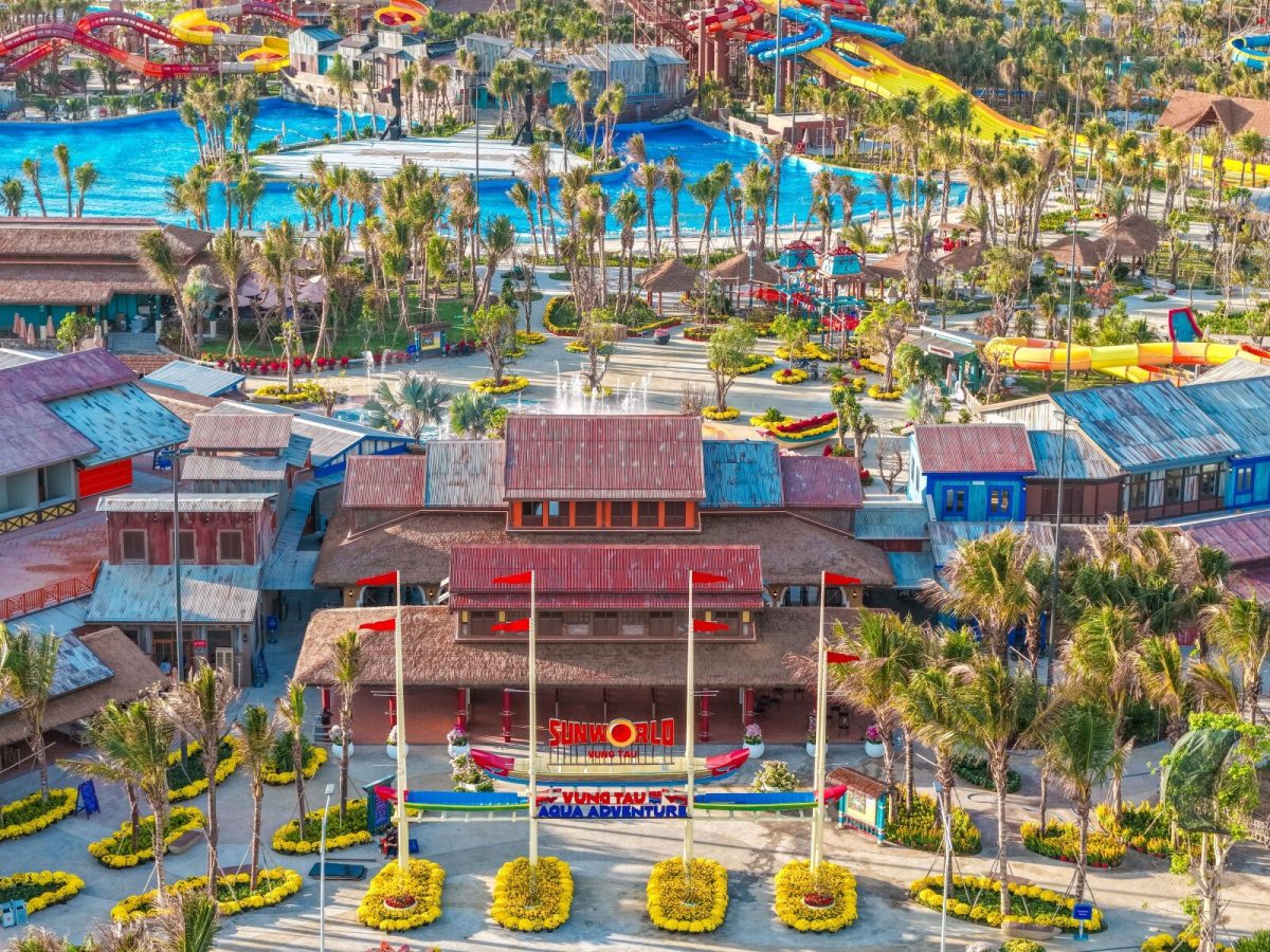 Aerial view of a colorful water park with blue slides, red stages, and yellow pool loungers surrounded by palm trees