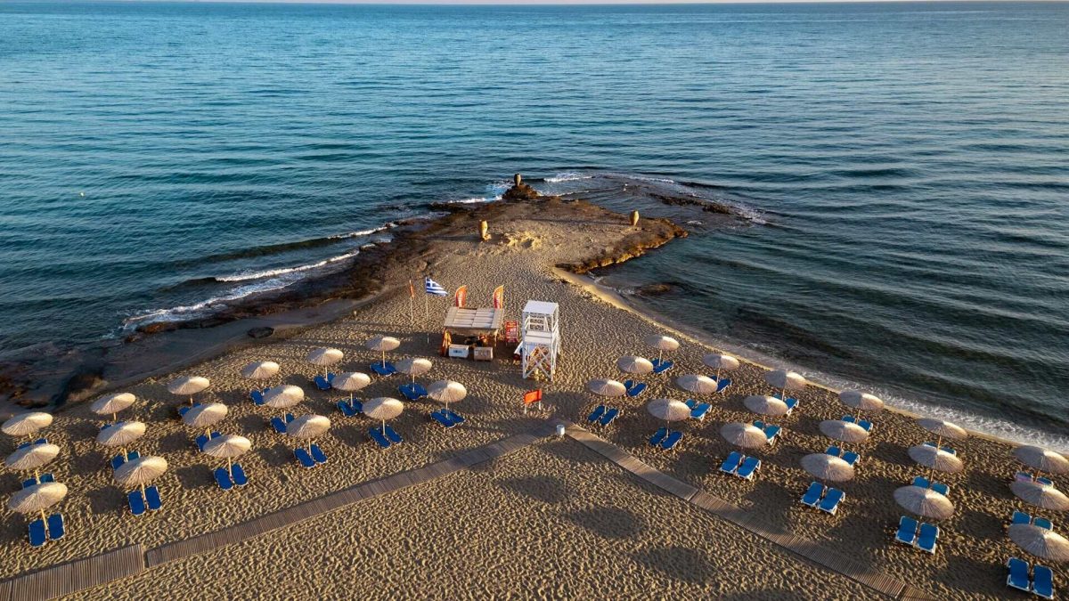 Aerial view of a crowded beach with numerous yellow and blue umbrellas and sunbeds lining the sand