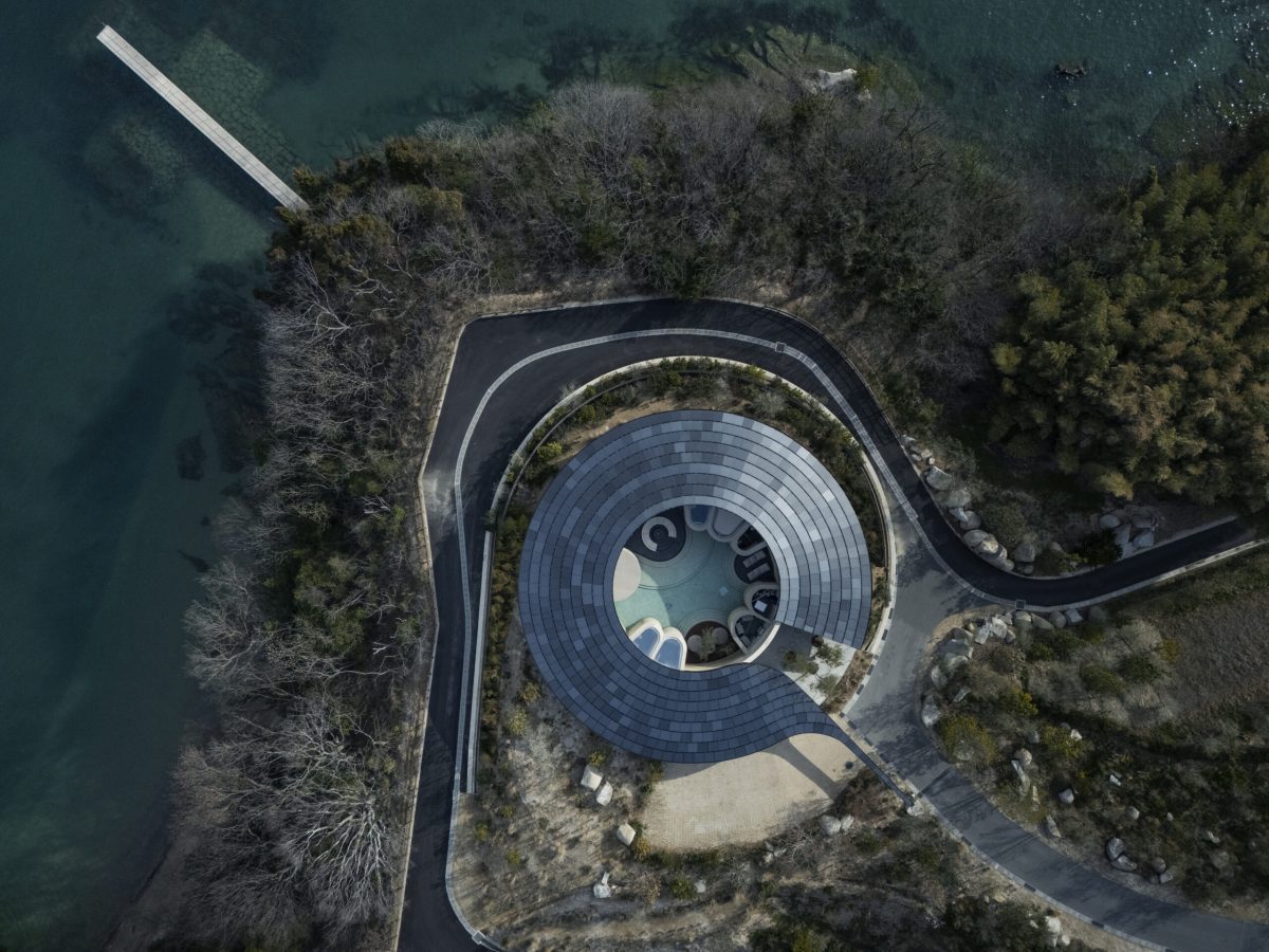 Aerial view of circular villa with rammed earth construction surrounded by forest and water