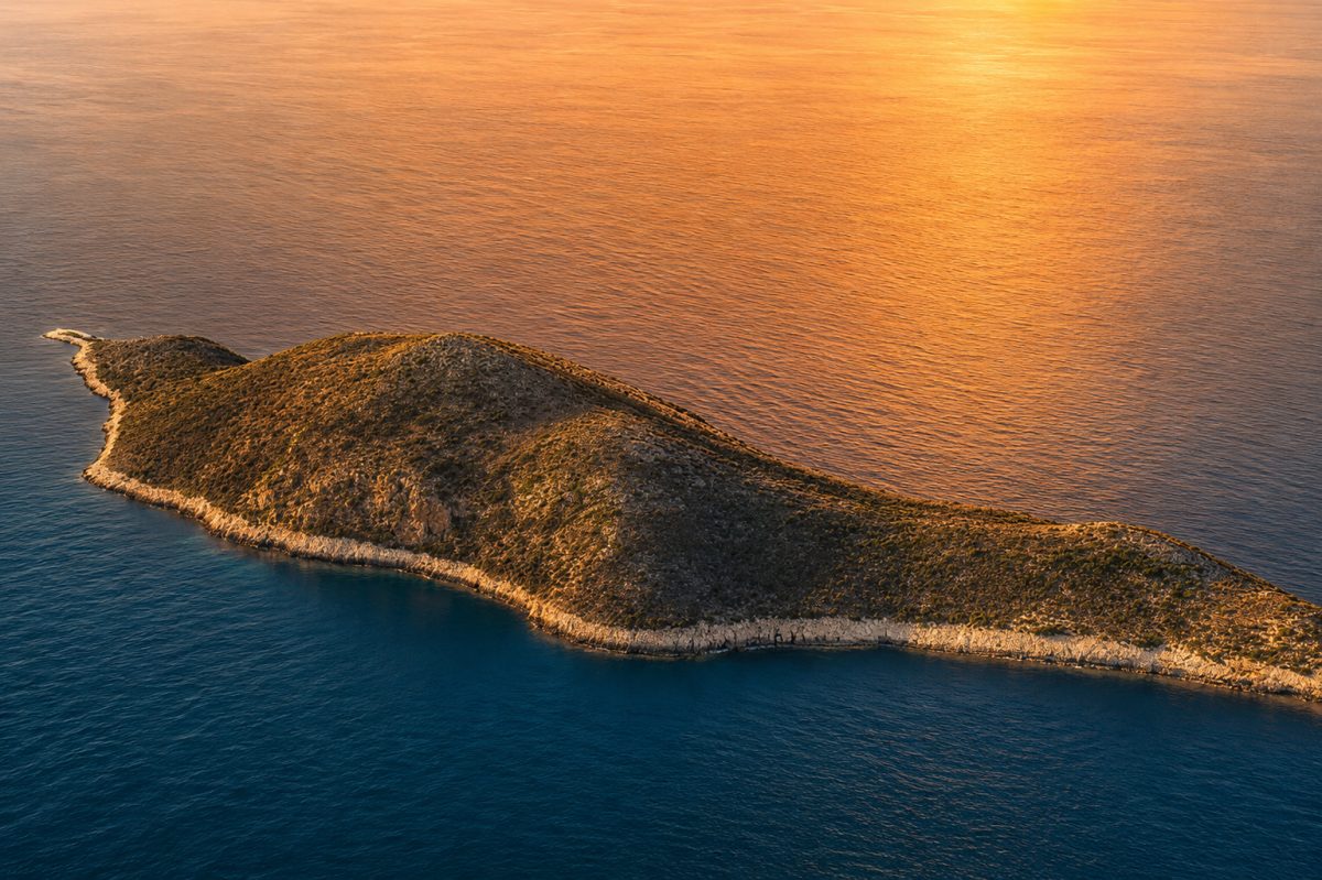 Aerial view of Makri island in the Ionian Sea at sunset with golden light reflecting on blue water