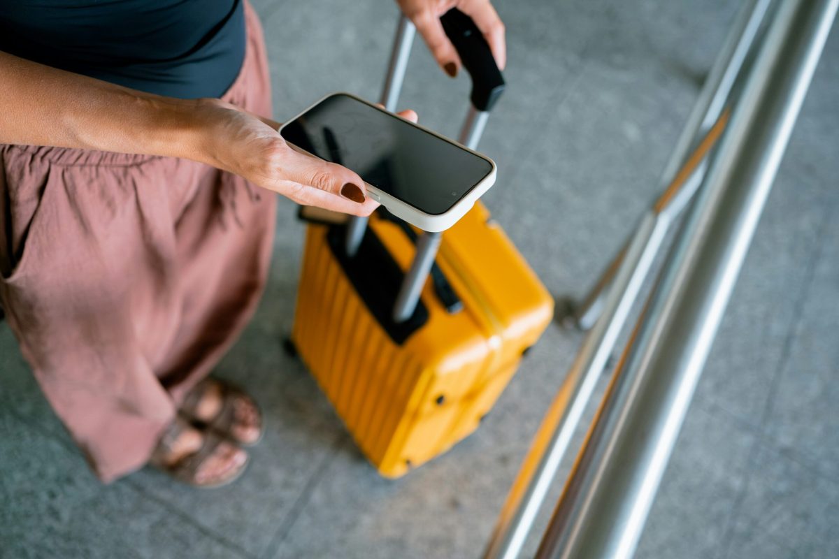 Traveler holding smartphone while pulling yellow luggage in airport