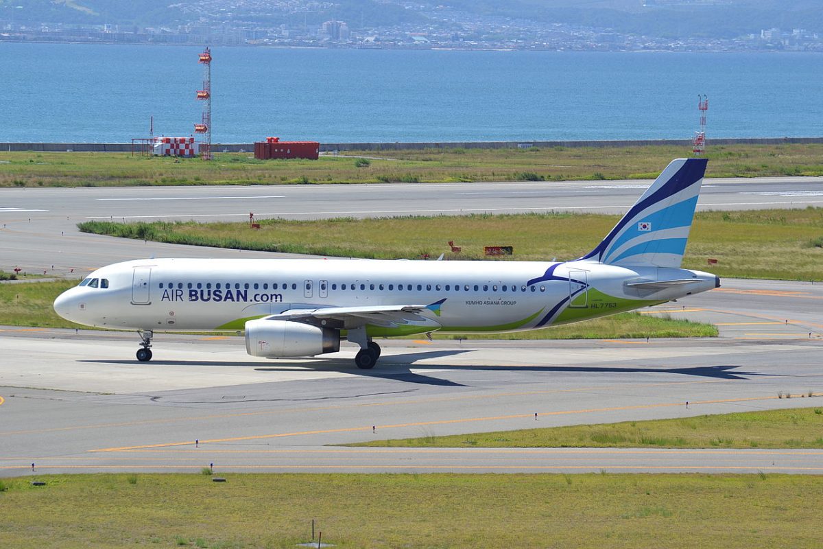 Air Busan aircraft on runway at airport with green taxiway and industrial facilities