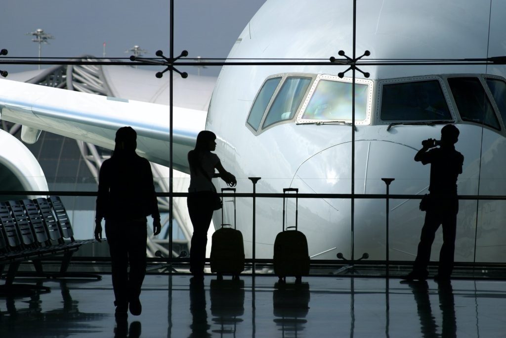 Silhouettes of travelers waiting in an airport terminal with aircraft visible through large windows