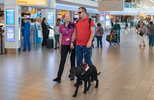 Airport staff member with service dog assisting passenger in terminal