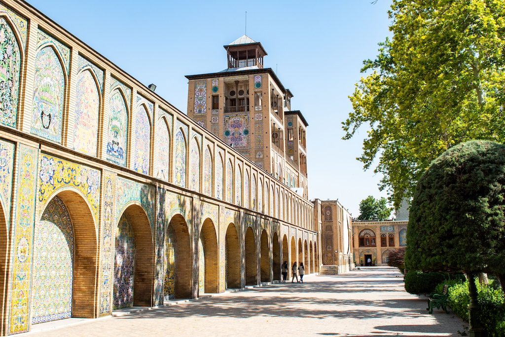 Historic palace courtyard with ornate arched colonnades and decorative tilework under blue sky