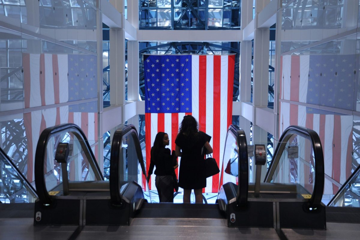 American flag displayed prominently in an airport terminal, with travelers in the foreground.