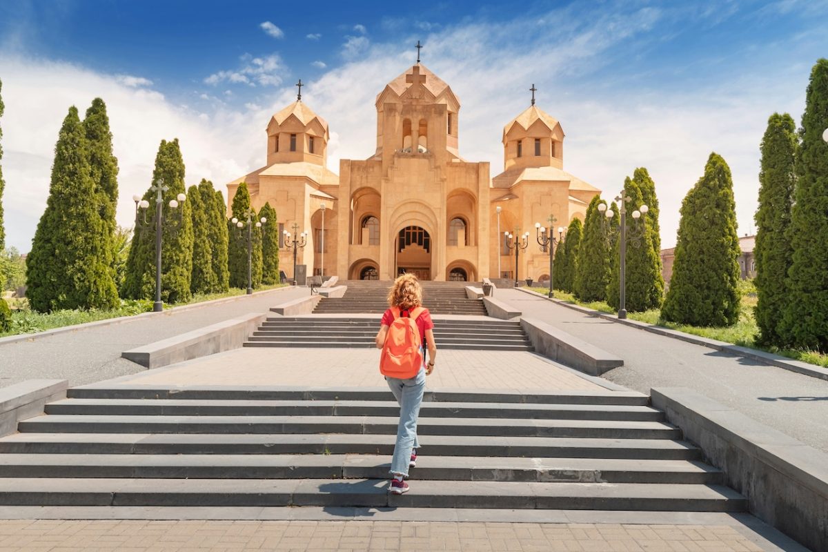 Visitor in orange shirt standing on steps facing St. Gregory of Illuminator Cathedral in Armenia