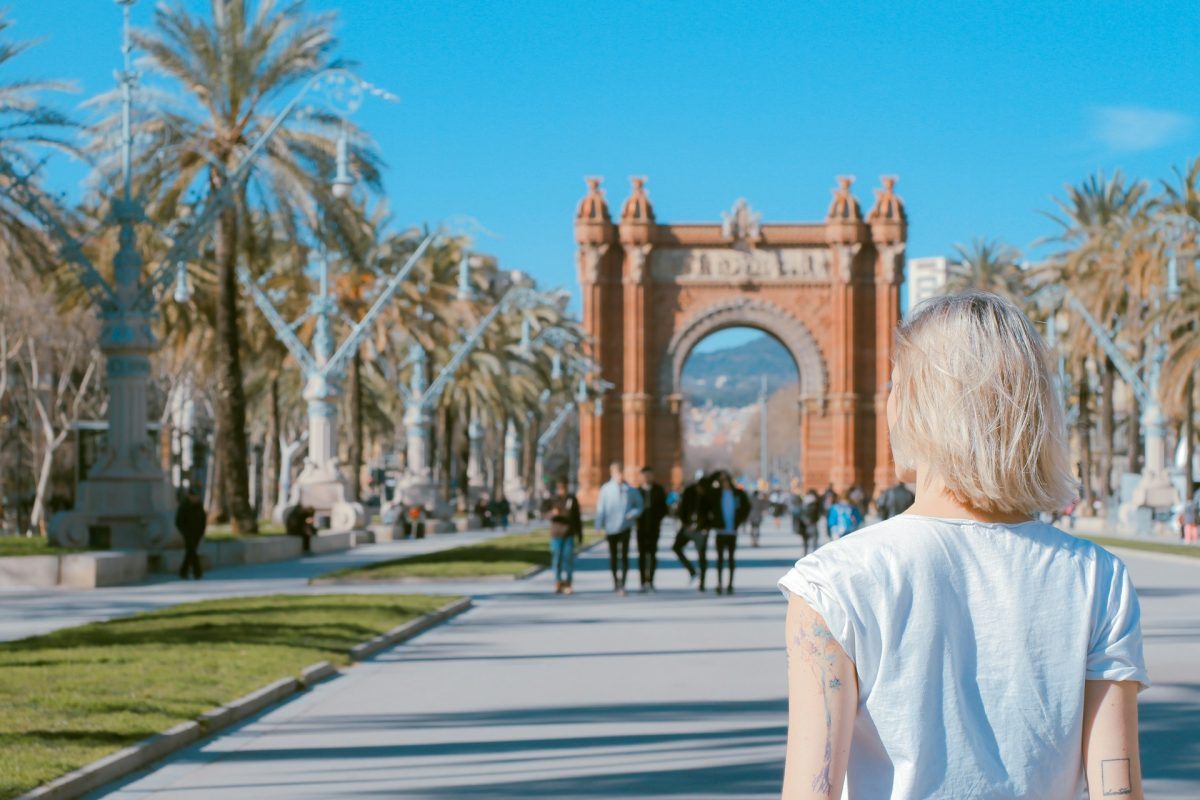 Tourist viewing Barcelona's Arc de Triomf with palm trees and clear blue sky