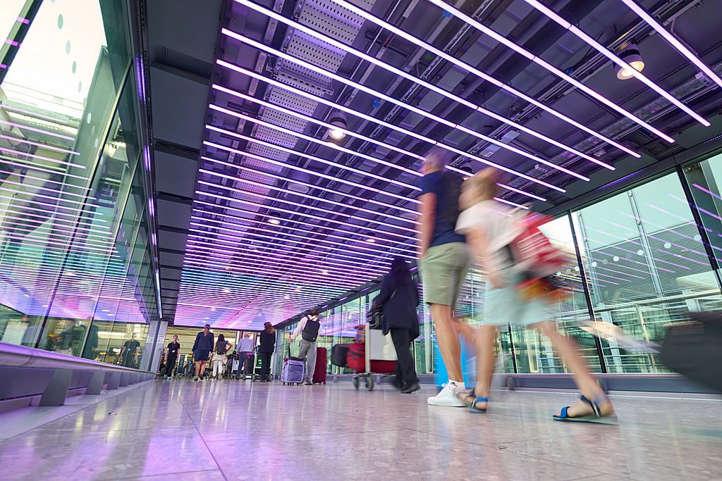 Modern airport terminal with purple lighting and travelers walking through spacious corridor
