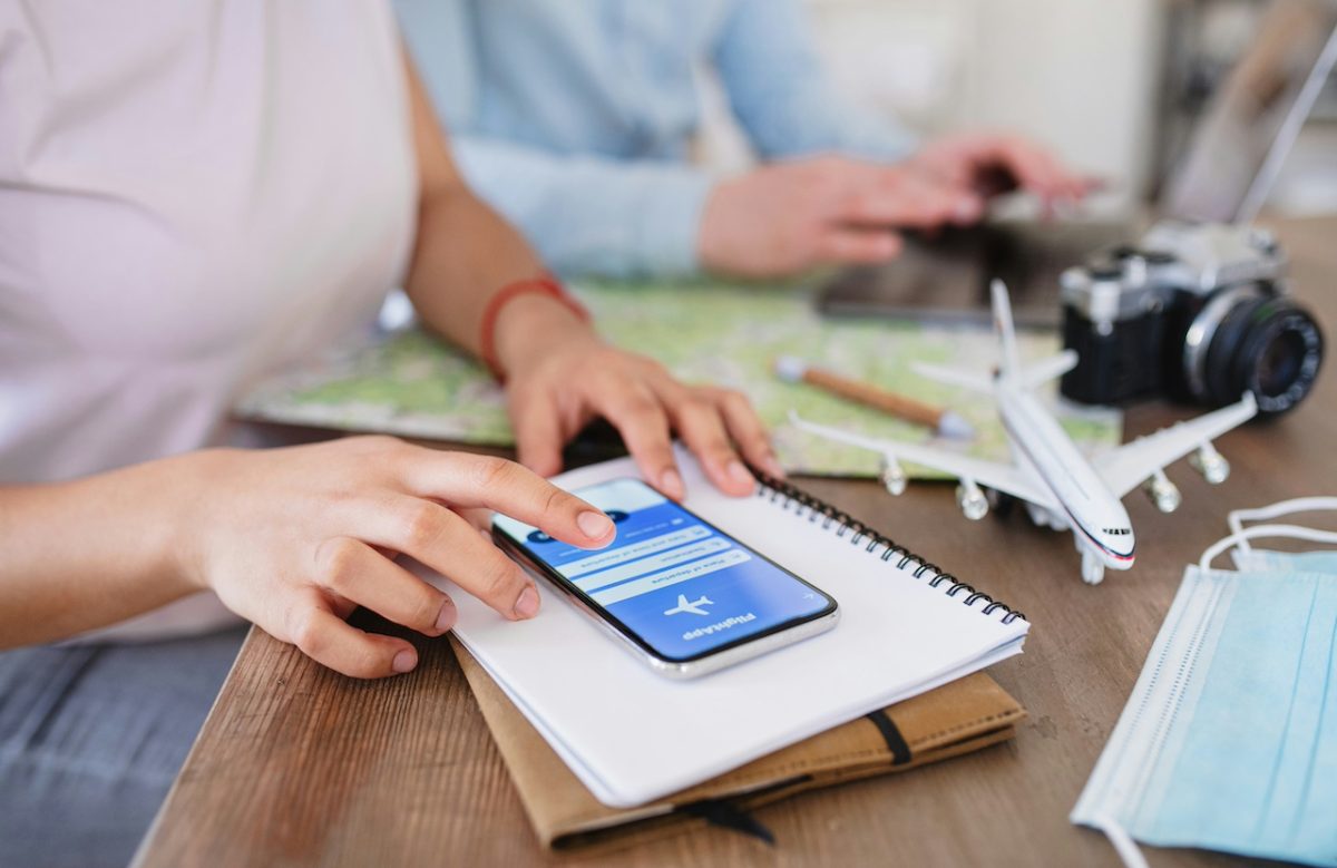 Person reviewing travel plans on smartphone with camera and documents on desk