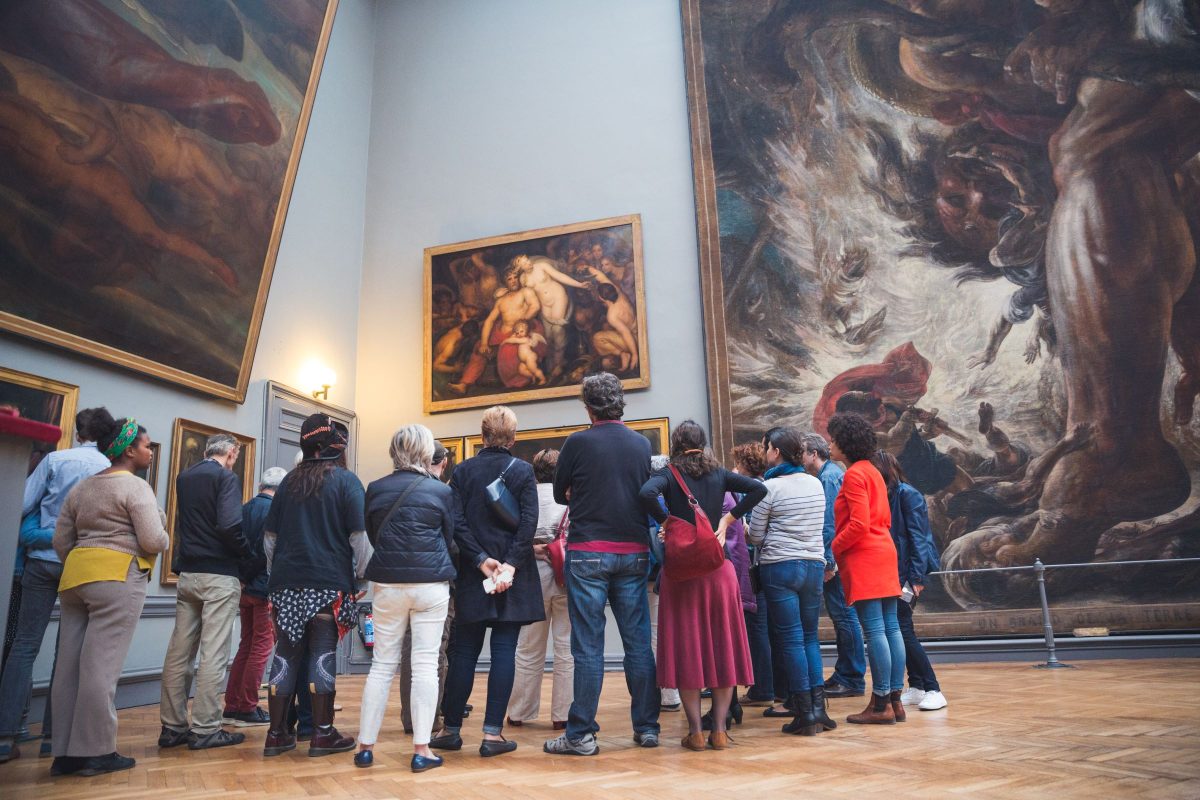 Visitors gathered in a museum gallery admiring large classical paintings on illuminated walls