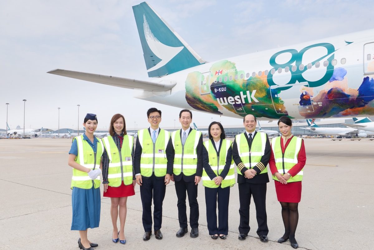 Cathay Pacific team members stand before Boeing 777 wrapped in colorful Hong Kong cultural artwork