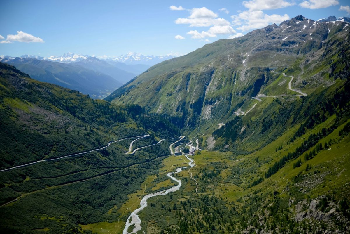 Aerial view of a winding mountain road through Swiss Alps valleys with green slopes