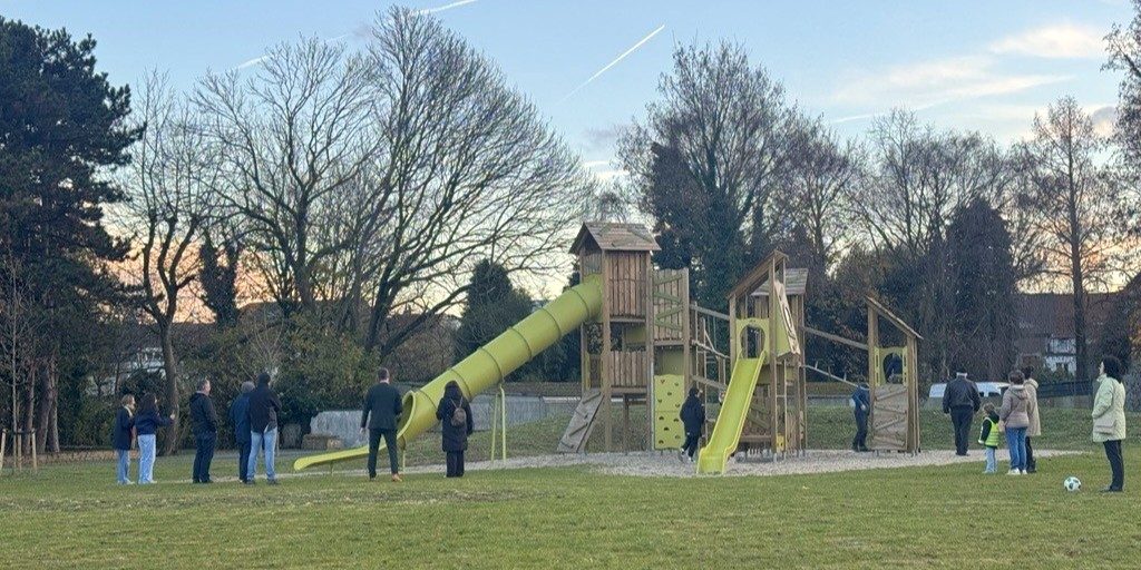 Children playing at a modern green playground with bright yellow structures in a spacious park