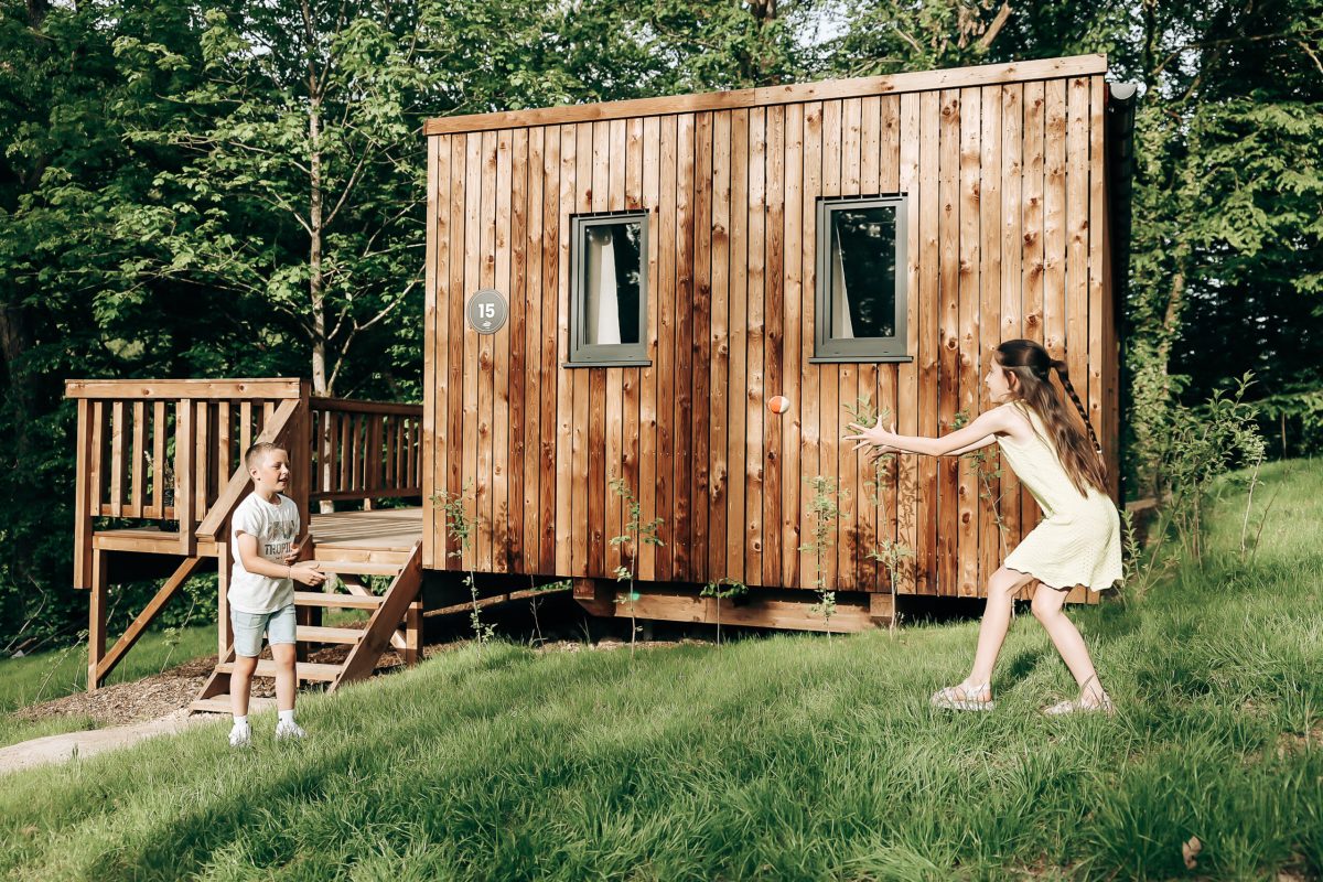 Children playing outside a wooden eco-lodge cabin surrounded by green trees