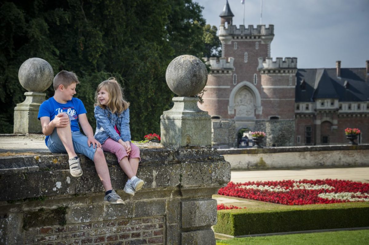 Children sitting on stone wall with castle and gardens in background