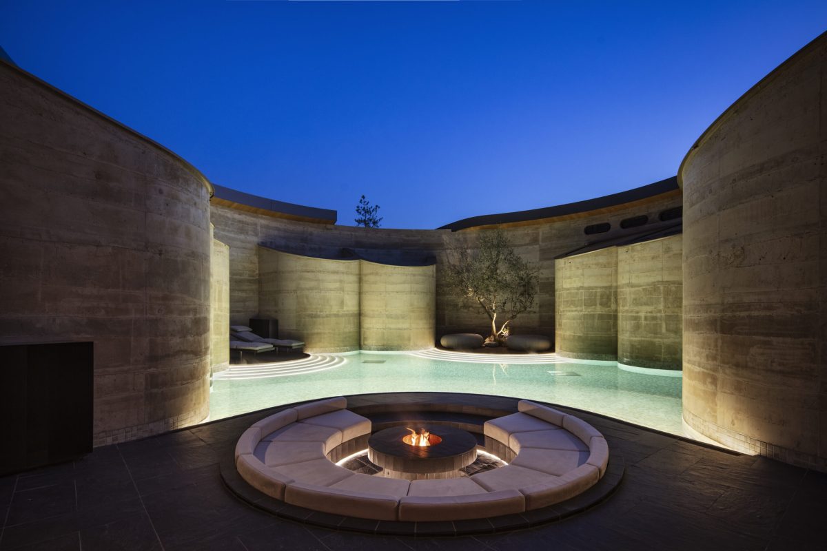 Circular fire pit courtyard surrounded by curved rammed earth walls with ambient lighting at dusk