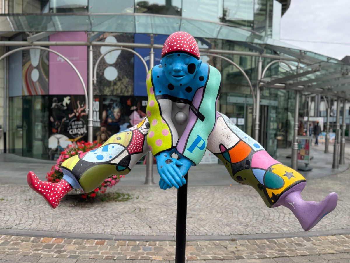 Colorful blue figure sculpture with pink hat and patterned arms in Spa town center
