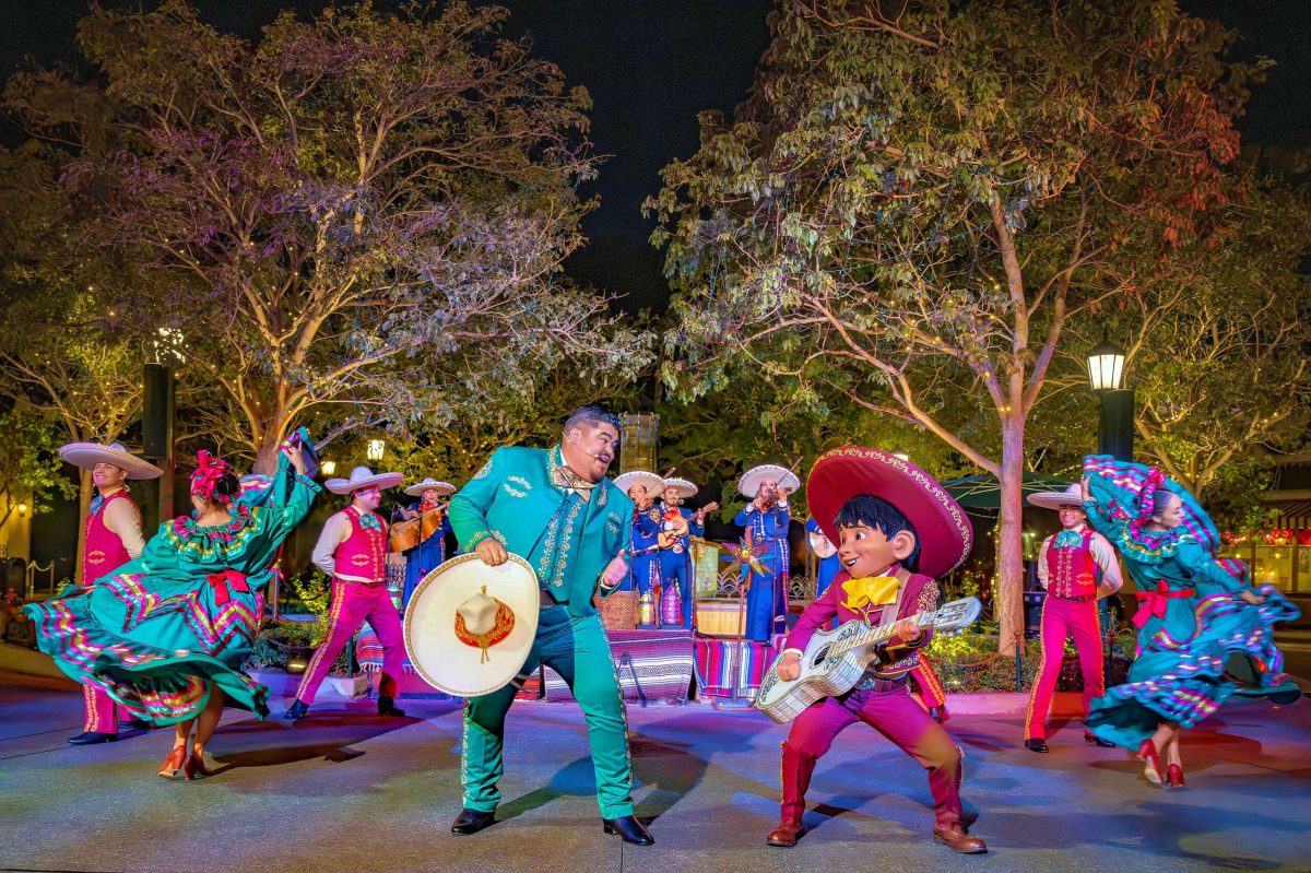 Colorful holiday characters perform on stage at night in a Disneyland park setting