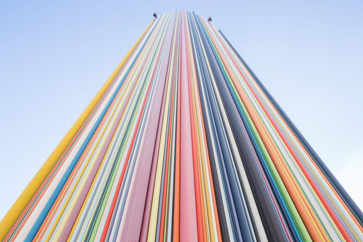 Colorful vertical stripes reaching toward clear blue sky, modern art installation