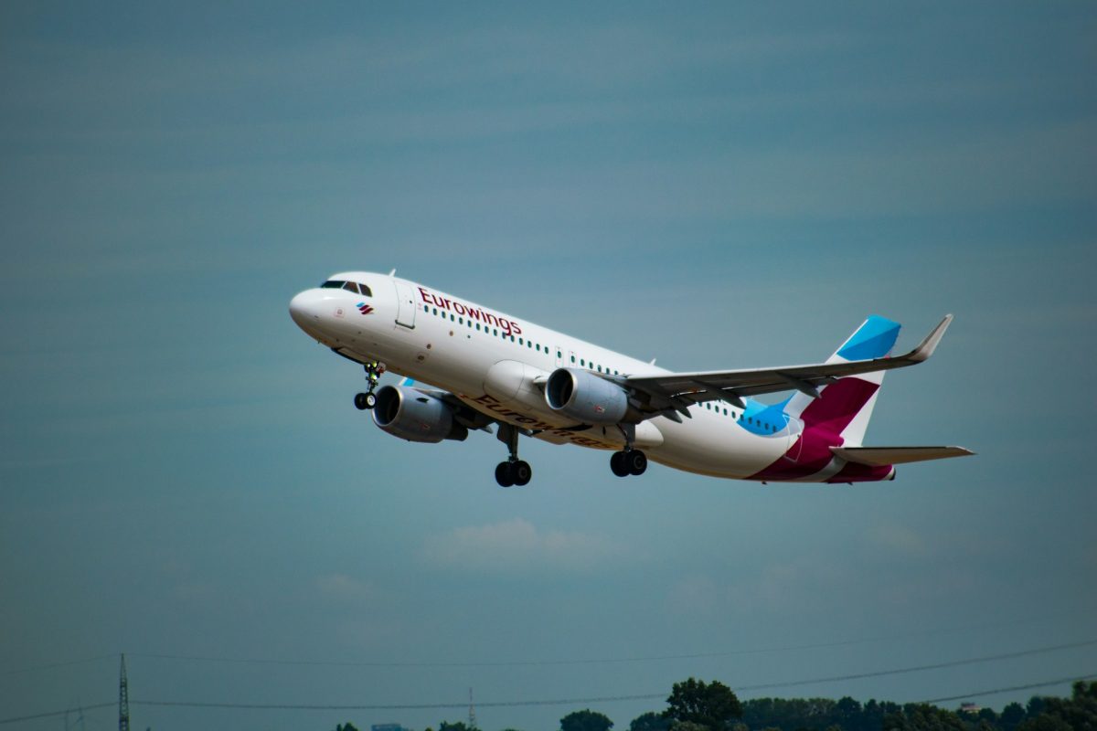 Commercial aircraft taking off against blue sky with trees visible below
