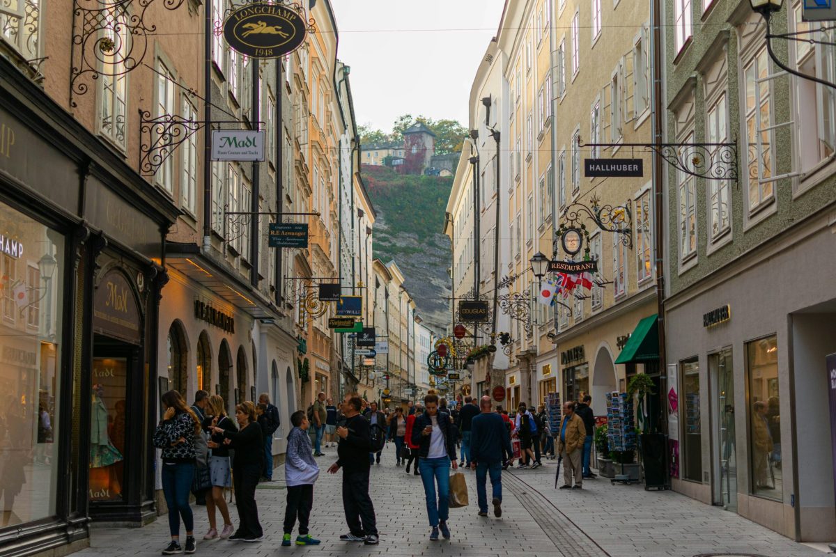 Crowded pedestrian shopping street in Salzburg's historic centre with castle visible on hilltop
