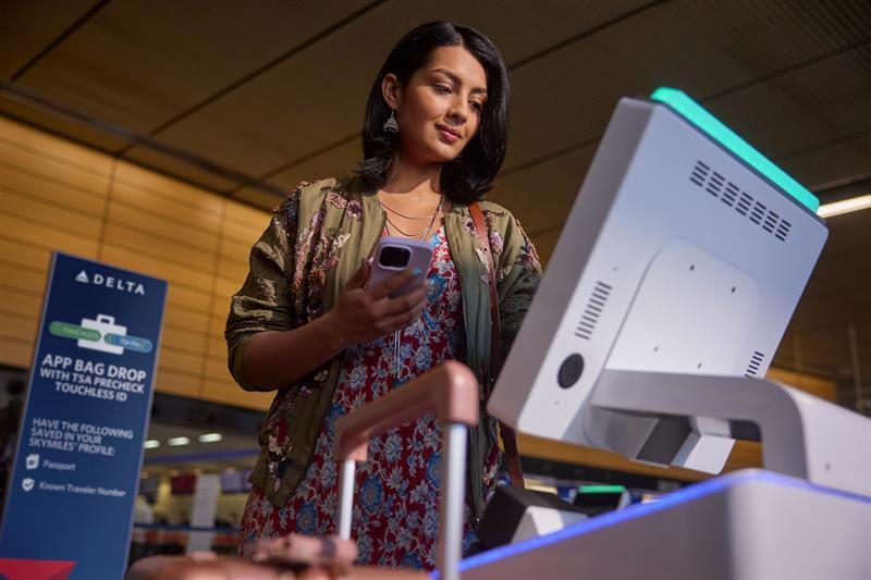 Delta Airlines employee at airport counter with baggage fee signage