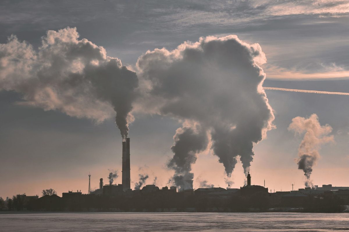 Industrial smokestacks release plumes of pollution into a hazy sky.