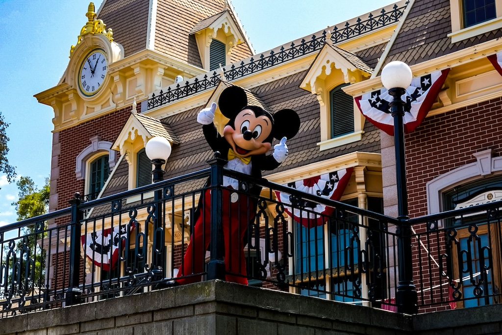 Mickey Mouse character on ornate building balcony with clock tower and golden decorations