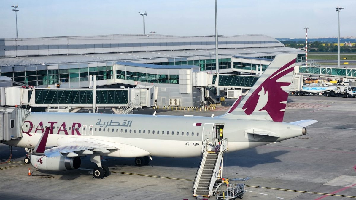 Qatar Airways aircraft at Doha airport gate with ground vehicles and terminal building