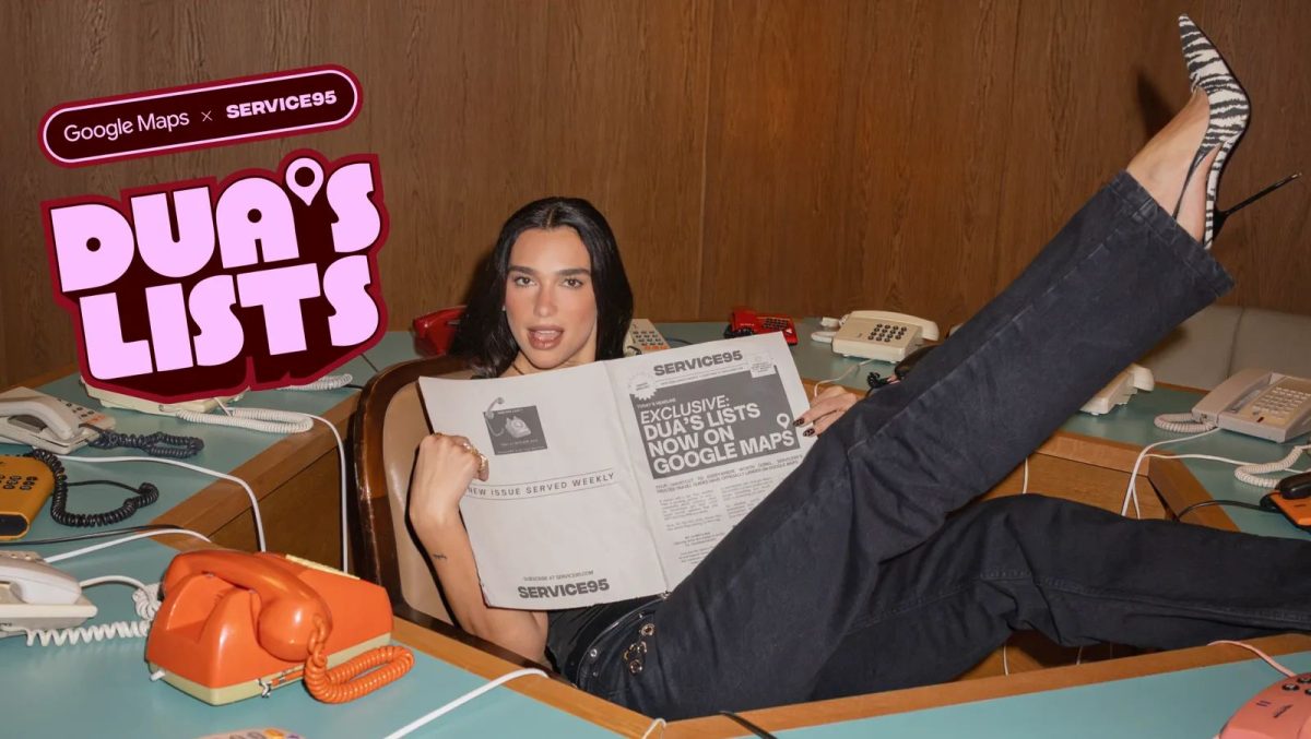Dua Lipa holds up a postcard while relaxing on a bed surrounded by travel maps