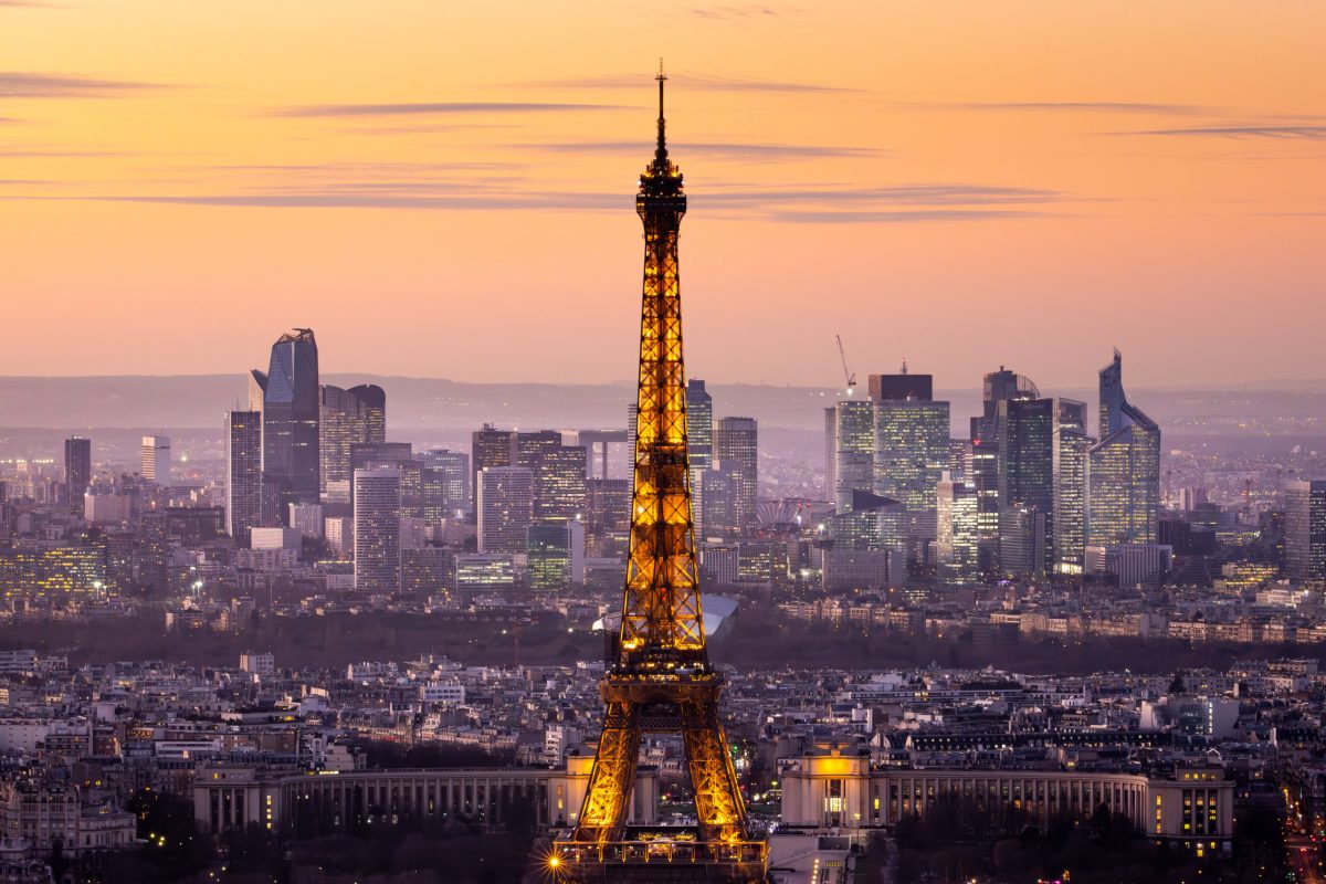 Eiffel Tower illuminated at dusk with Paris skyline behind it at golden hour