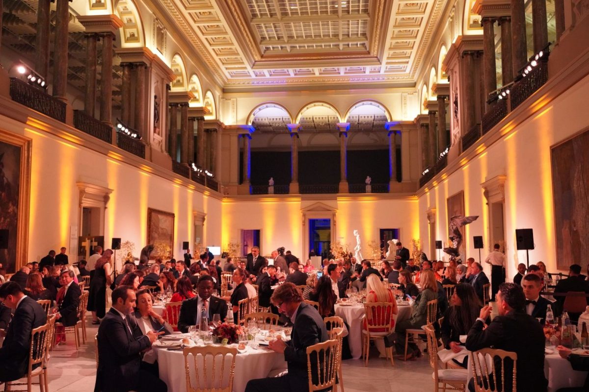 Elegant gala dinner in ornate hall with guests at round tables under golden lighting