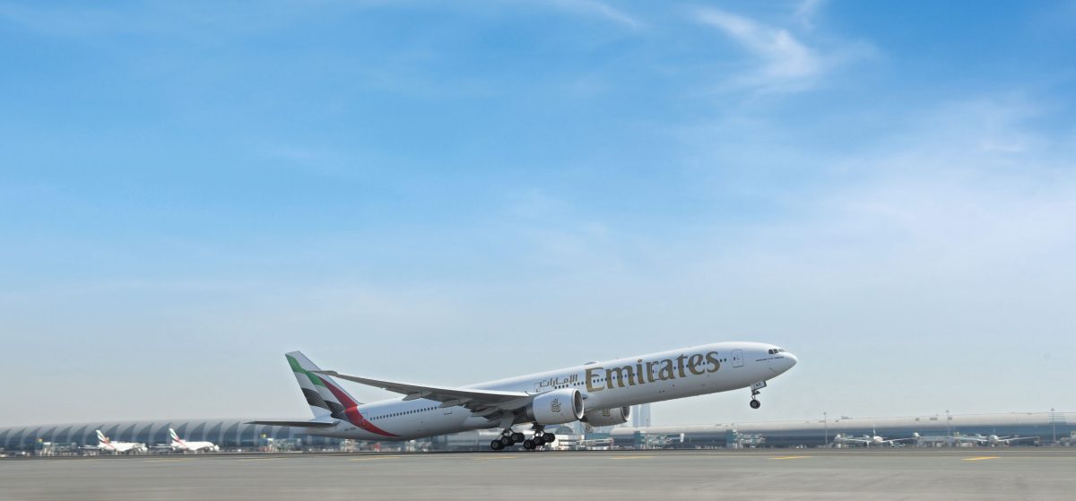 Emirates aircraft taking off on sunny runway with clear blue sky