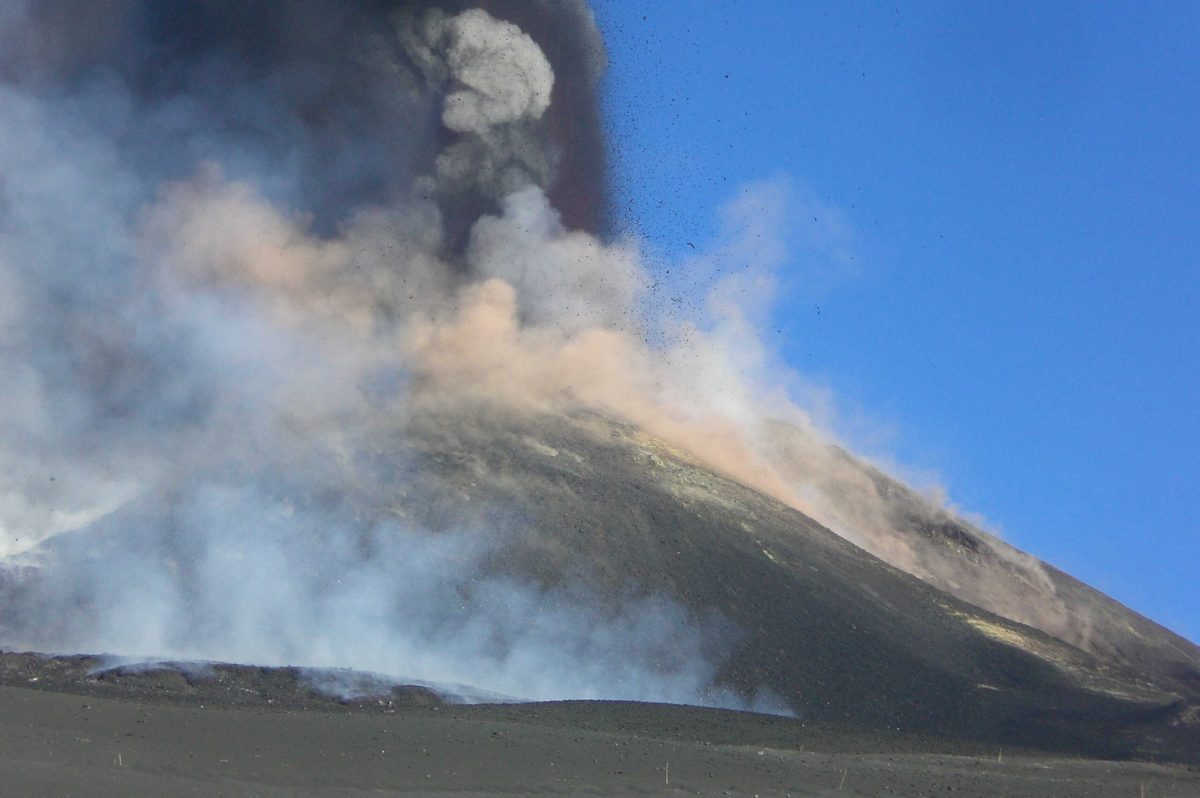 Mount Etna erupts, sending a plume of ash into the clear blue sky.