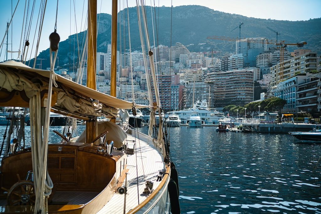 Wooden sailboat moored in Mediterranean harbor with coastal city and mountains in background