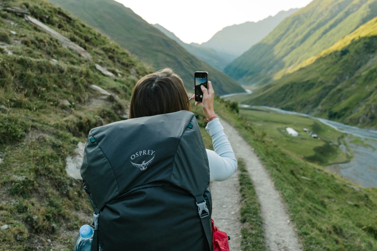 Hiker taking a photo of a mountain valley landscape while on a hiking trail