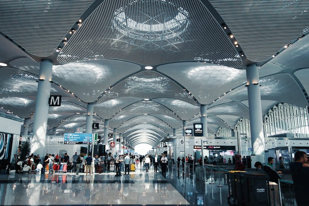 Modern airport terminal with soaring ceiling, abundant lighting, and crowds of travelers
