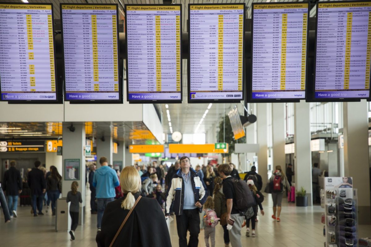 Crowded airport terminal with departure boards overhead and travelers moving through the hall