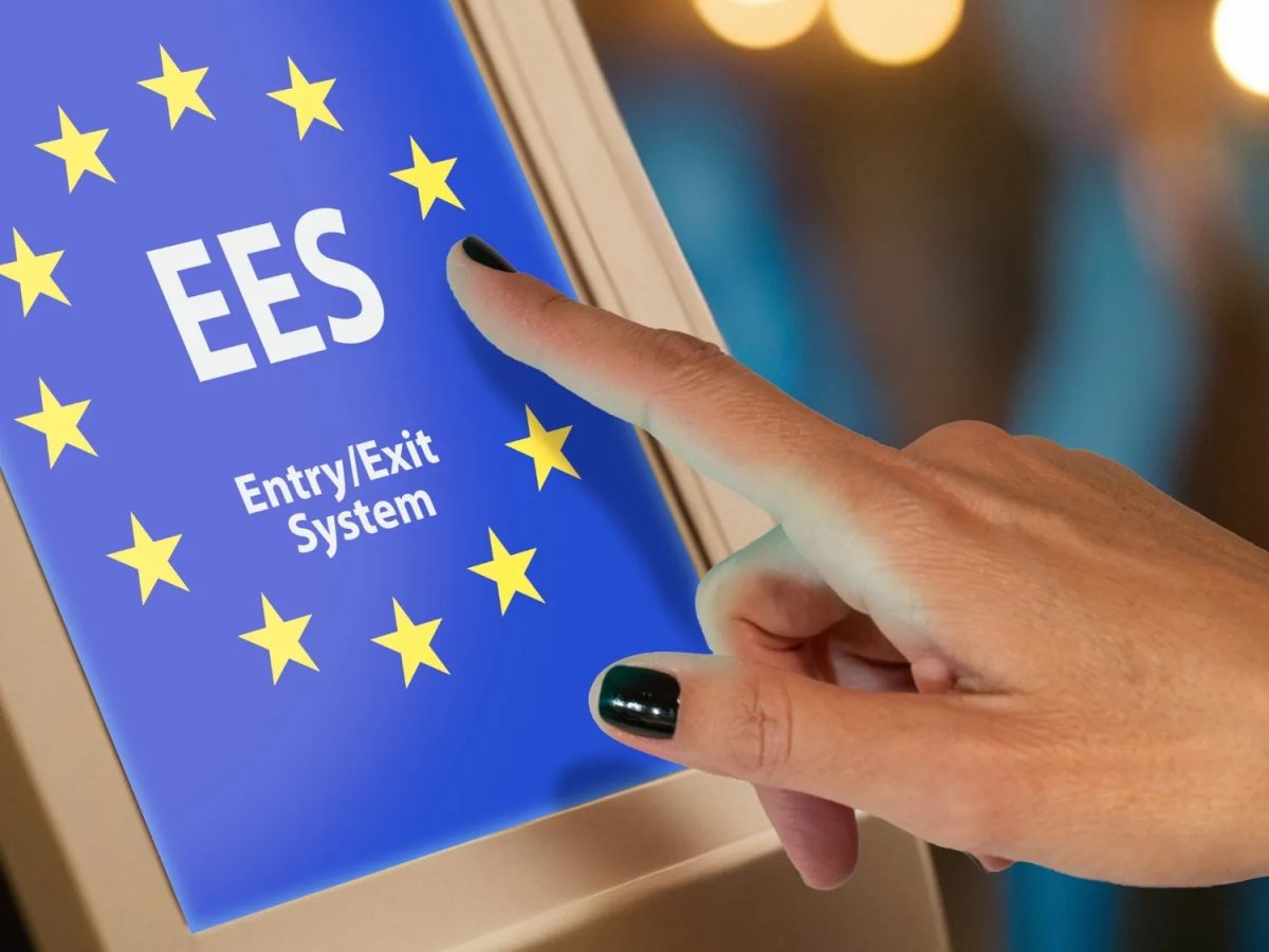 Hand touching EES Entry/Exit System screen with EU stars at airport border control