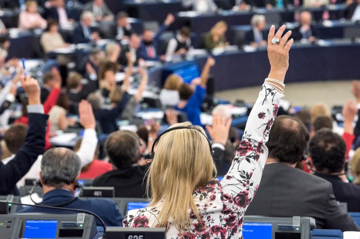 Woman raising hand to vote in European Parliament chamber