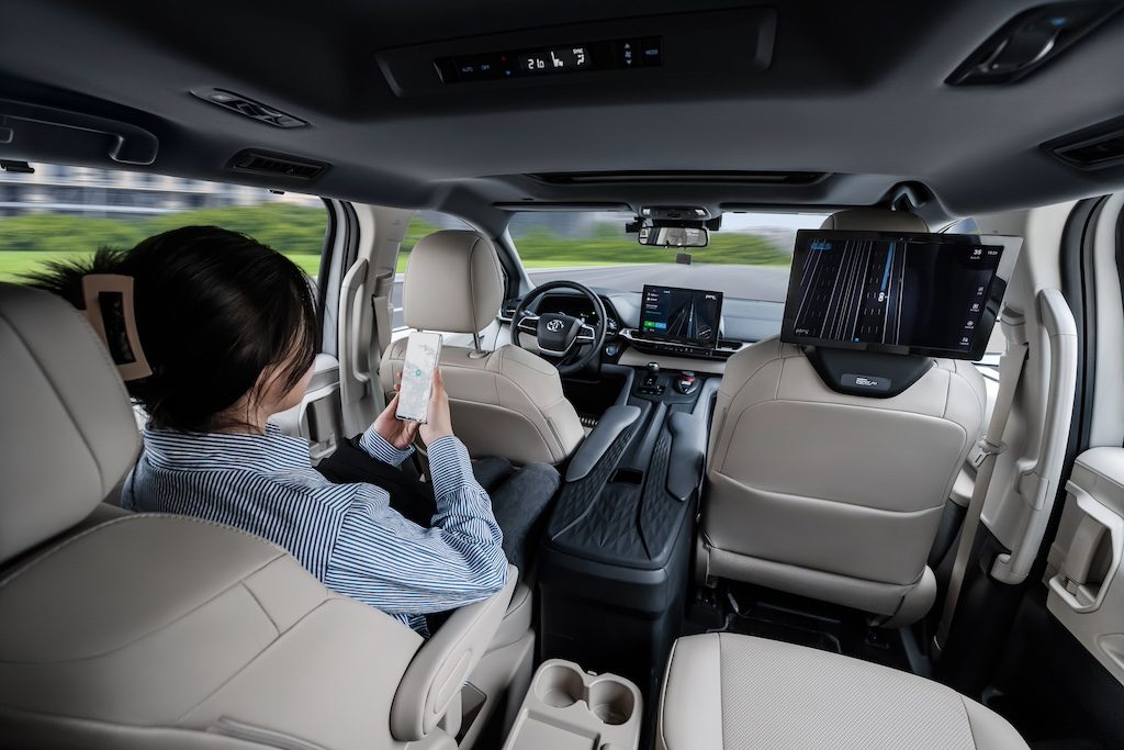 Interior of autonomous vehicle with passenger holding tablet, hands-free driving displayed
